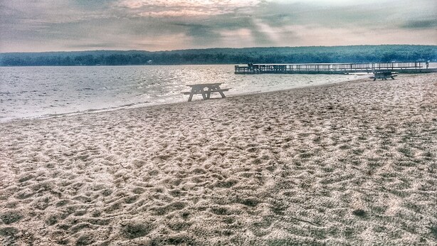 Een strand met een houten bankje en een pier die het water in reikt.