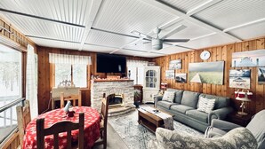 Een gezellige woonkamer met een open haard, houten wanden, een eettafel met een rode tafelkleed en een bank.