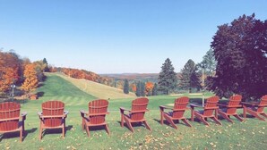 Een rij houten Adirondack-stoelen op een grasheuvel, met uitzicht op een golfbaan en herfstbomen.
