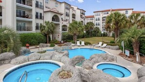 Un hôtel doté de plusieurs piscines, entouré de grands rochers, de palmiers et de chaises longues.