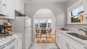 Eine moderne Küche mit weißen Schränken, ein Essbereich mit Tisch und Stühlen sowie ein großes Fenster mit Blick ins Freie.