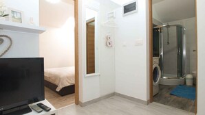Camera d'albergo compatta con letto, televisore, lavatrice e angolo doccia.