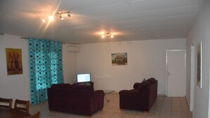 A living room with two dark sofas, a wooden dining table, and a television. - FURNISHED HOUSE COSY (Libreville)