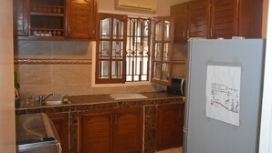 A kitchen with wooden cabinets, a marble countertop, a sink, and an air conditioner. - FURNISHED HOUSE COSY (Libreville)