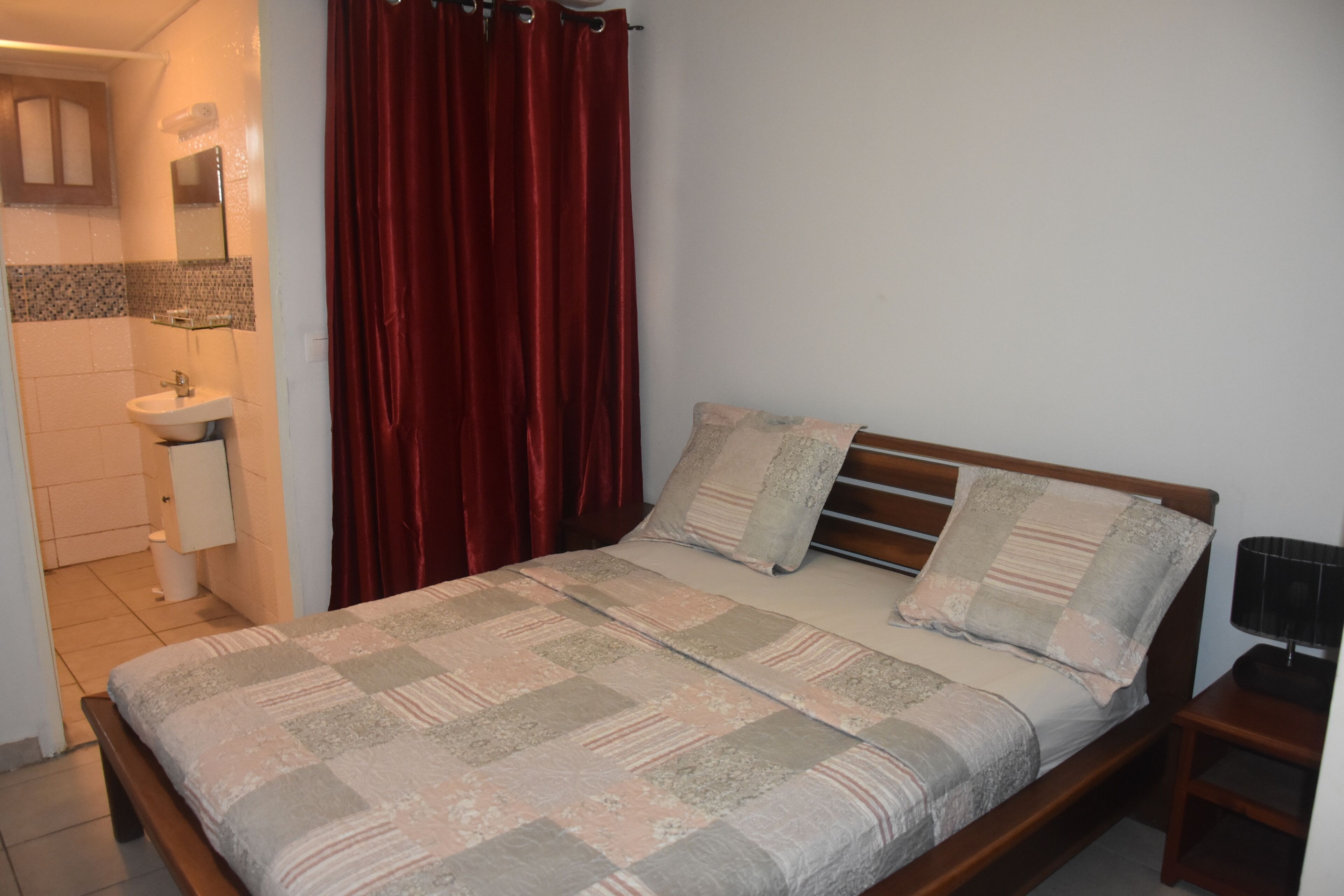 A bedroom with a bed, a nightstand, a wooden headboard, a red curtain, a white sink, and a mirror.