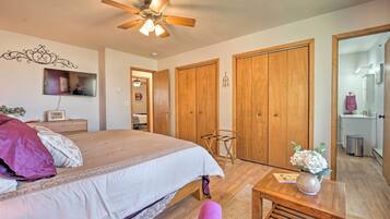 Un dormitorio con cama, armario de madera, una mesita con un florero y un ventilador de techo.