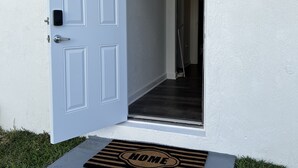 Uma porta branca com um tapete de entrada com a palavra 'HOME' e uma pequena janela acima.