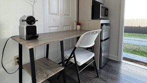 Cozinha compacta com micro-ondas, geladeira e uma pequena mesa com cadeira.