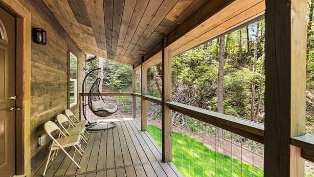 A wooden deck with a hanging chair, a table, and a view of a forest.