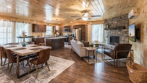 A spacious cabin interior with a dining area, kitchen, living room, and fireplace.