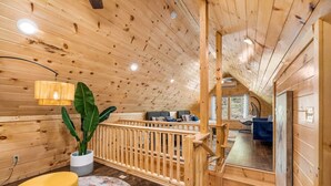 A wooden interior with a staircase leading to an upper level, a seating area with a sofa and a dining table, and a potted plant.