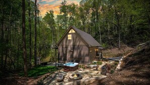 A cabin with a stone fire pit and hot tub in a forest setting.