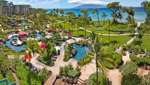 Ein Resort mit mehreren Schwimmbecken, üppiger Bepflanzung und Blick auf das Meer.