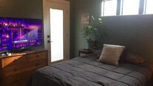 A bedroom with a bed, a dresser, a television displaying a cityscape, a potted plant, and a window with blinds. - Walk to the crystal clear San Marcos river (San Marcos)