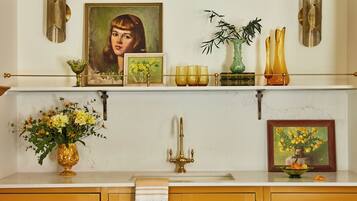 A kitchen with a white countertop, gold fixtures, and decorative items including a vase, a framed painting, and a Buddha statue.