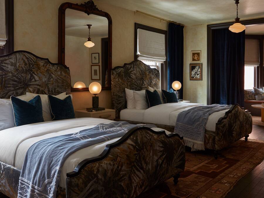 A hotel room with two large beds, a large mirror, bedside lamps, and a view of the outside.