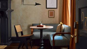 A room with a round table, a chair, a sofa, a fireplace, and a door with a number.