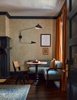 A room with a round table, a chair, a sofa, a fireplace, and a door with a number.