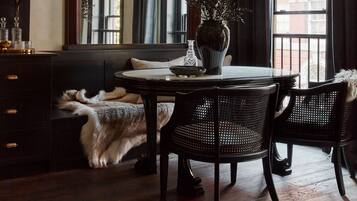 A room with a round table, two chairs, a large mirror, a fur throw, and a window with curtains.