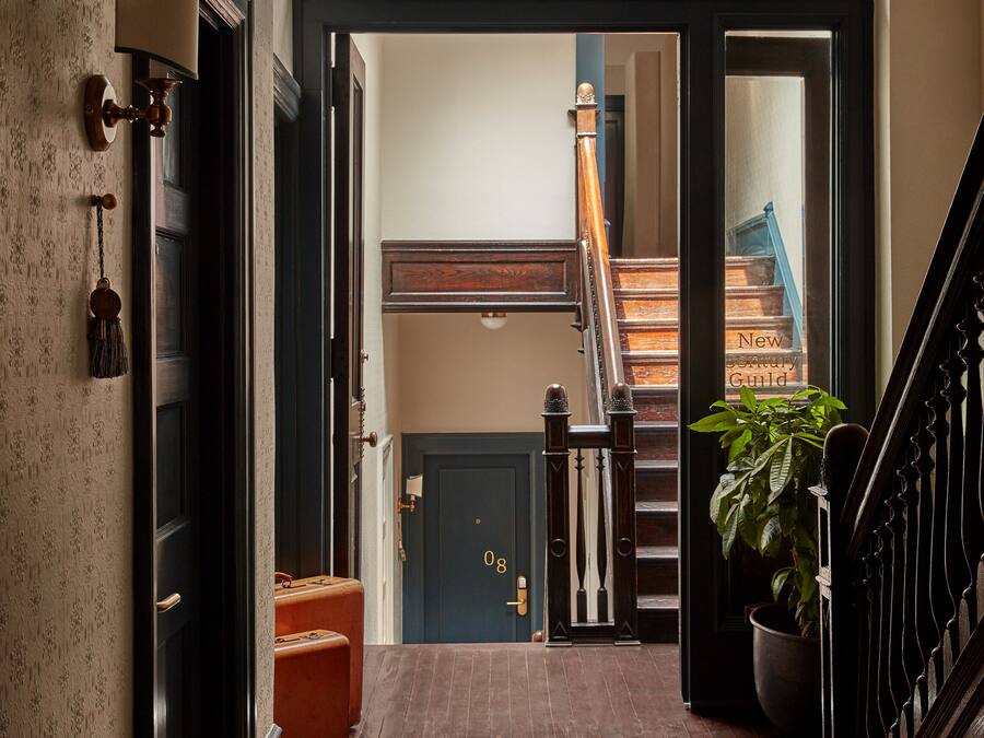 A hallway with a patterned rug, a wooden bench, and a staircase leading to an upper floor.