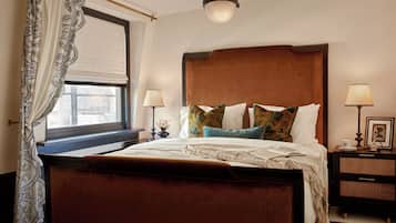 A bedroom with a large bed, two bedside tables, a window with curtains, and a hanging light fixture.
