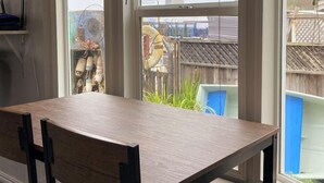 Un comedor con una mesa y sillas de madera, ventanas amplias con persianas y vistas al jardín trasero.