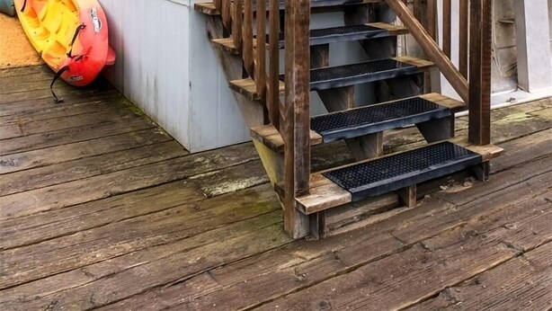 Una casa con escaleras de madera que dan a un porche, un kayak y una tabla de remo.