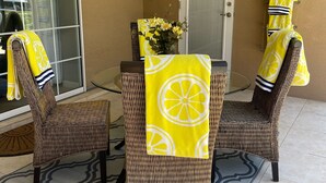 A patio with wicker chairs and a table, a door, and a window with a view.