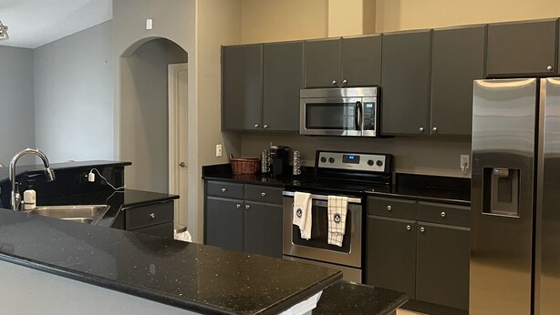 A modern kitchen with grey cabinets, stainless steel appliances, and a black granite countertop.