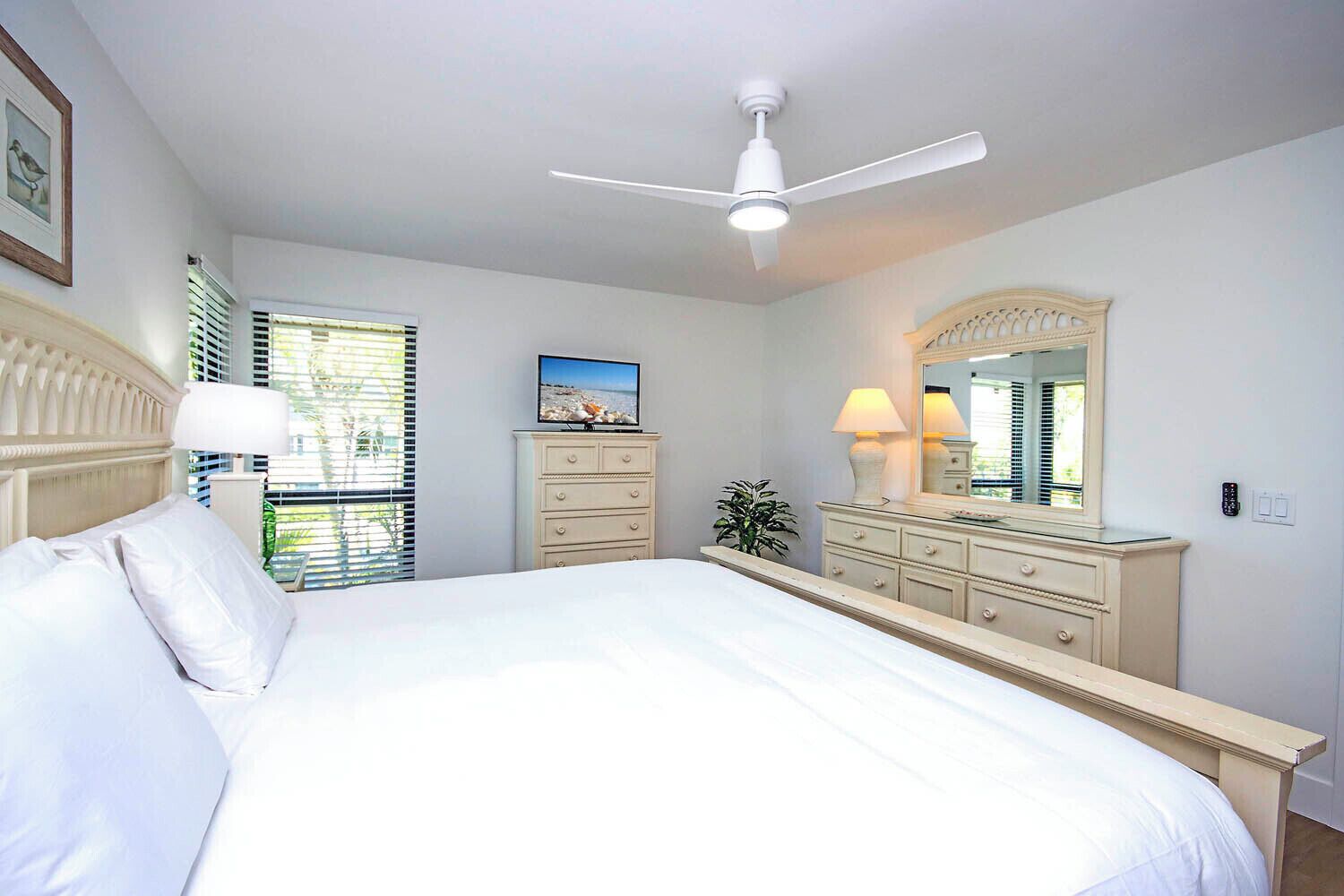 A bedroom with a large bed, a ceiling fan, a dresser, a mirror, and a television.