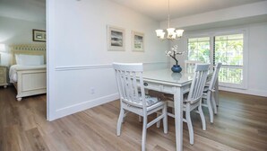 A dining area with a white table and chairs, a chandelier, and a view through a window.