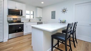 A modern kitchen with white cabinetry, a built-in oven, a microwave, and a large island with bar stools.