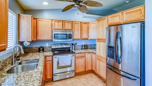 Une cuisine dotée de meubles en bois, d’un four à micro-ondes, d’une cuisinière, d’un réfrigérateur, de plans de travail en granit et d’un ventilateur de plafond.