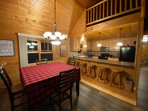 Cozy cabin interior with a dining area, kitchen, and sloped ceiling with exposed beams.