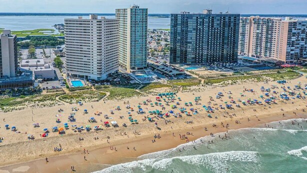 A beach with numerous umbrellas and people, surrounded by high-rise buildings.