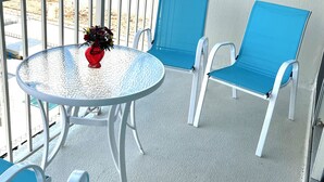A balcony with a round table and blue chairs, overlooking a beach.