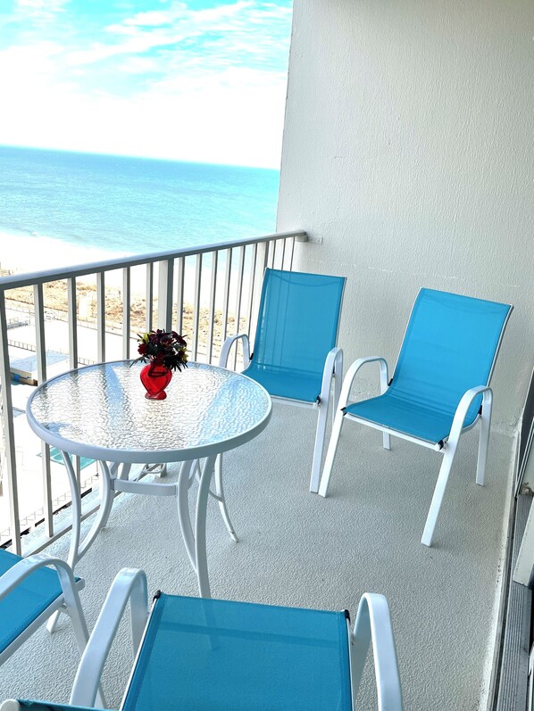 A balcony with a round table and blue chairs, overlooking a beach. - The Quay, Beach Front Building with Pools & Much More.... (Ocean City)