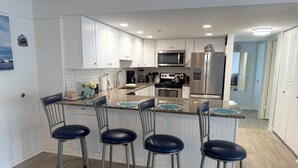 A modern kitchen with white cabinets, stainless steel appliances, and a bar area with stools.