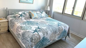 A neatly made bed with a starfish and leaf pattern, a bedside lamp, and a window with curtains.