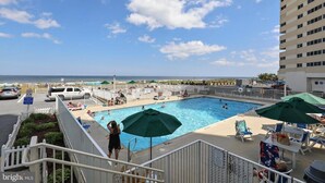 A rooftop pool with a view of the ocean, surrounded by lounge chairs and umbrellas.