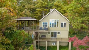 A two-story house with a balcony and a covered area, surrounded by dense trees and foliage.