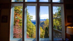 A room with a large window overlooking a scenic view of autumn foliage and mountains.