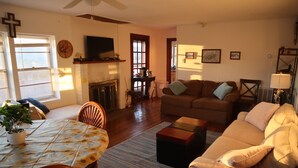 A living room with a fireplace, a sofa, a dining table with chairs, and a television mounted on the wall.