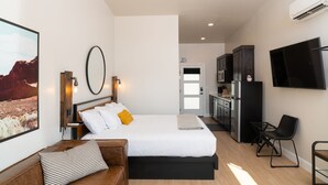 Una habitación de hotel moderna con una cama grande, un escritorio, una kitchenette y un televisor montado en la pared.