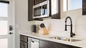 Una cocina moderna con armarios oscuros, un lavamanos de acero inoxidable, un microondas y un lavavajillas.
