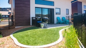 Una casa moderna con un patio que incluye una parrilla, mobiliario exterior y un césped cuidado.