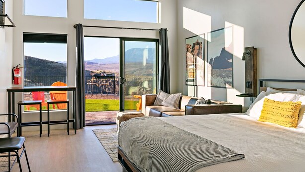 A bedroom with a large bed, a desk, and a balcony with a view of mountains. - Amazing View #1 Pet Friendly (La Verkin)