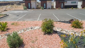 Een parkeerplaats met twee gebouwen, een grindpad met beplanting en een bergachtige achtergrond.