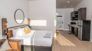 Un dormitorio moderno con una cama grande, mesitas de noche, un espejo y vistas a la cocina.