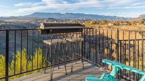 Un balcón con vistas a montañas, una parrilla y dos taburetes de bar.